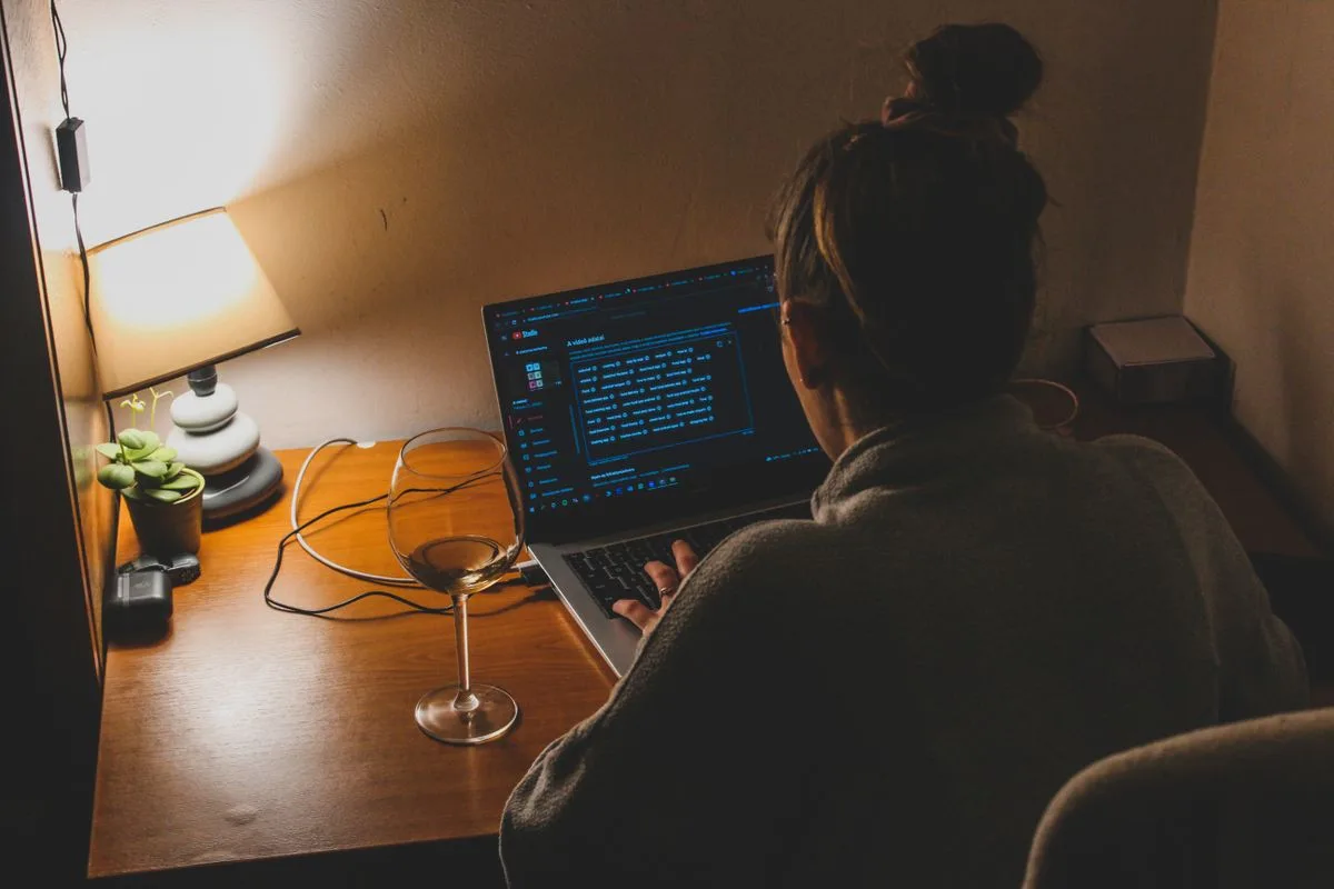 Una mujer trabajando sola de noche en su escritorio, iluminada por una lámpara y la pantalla del portátil