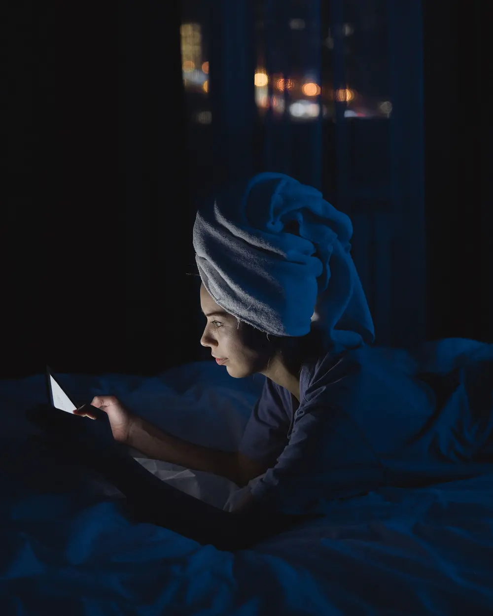 Una mujer leyendo su celular en la cama de noche, iluminada solo por la pantalla