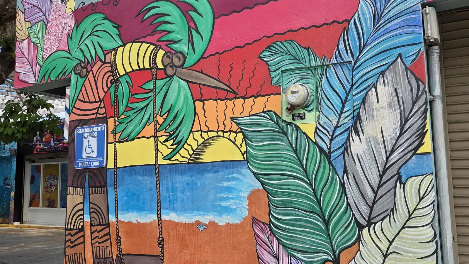 Mural of a palm tree with a rope swing and a sunset over the sea, painted on a wall in the town center of Isabela, Puerto Rico.